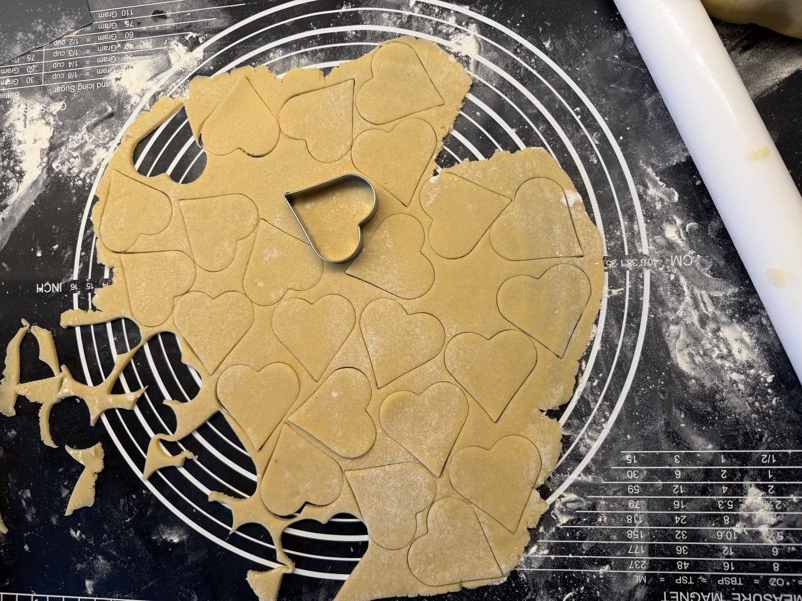 Ausgerollter Butterplätzchenteig mit ausgestochenen Herzen auf einer Backmatte