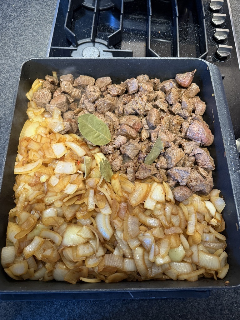 Angebratene Rindfleischwürfel, angeschwitzte Zwiebeln und Lorbeerblätter im Gourmet-Bräter