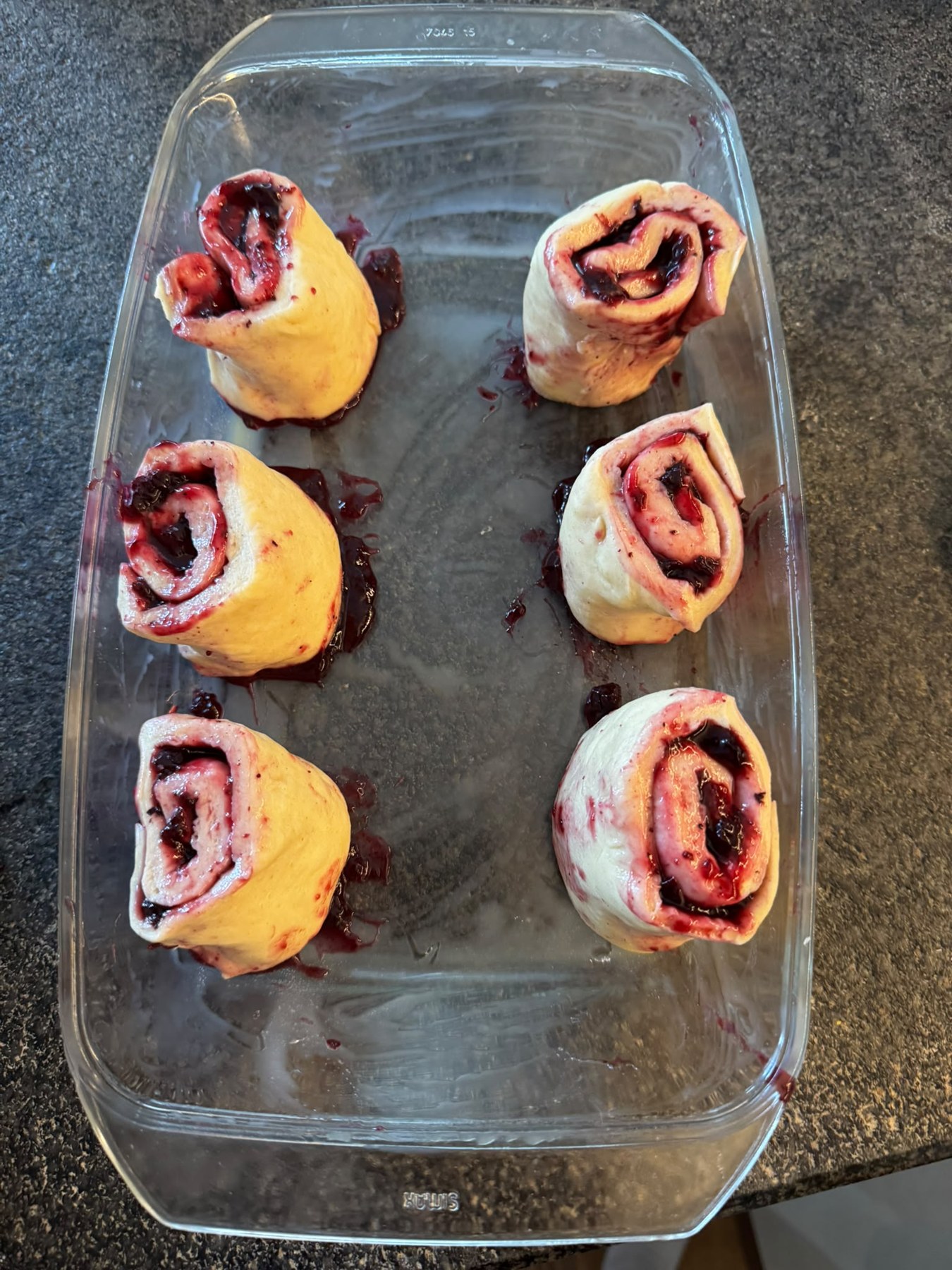 Sechs ungebackene Blaubeerschnecken mit Marmeladenfüllung in einer Glasform