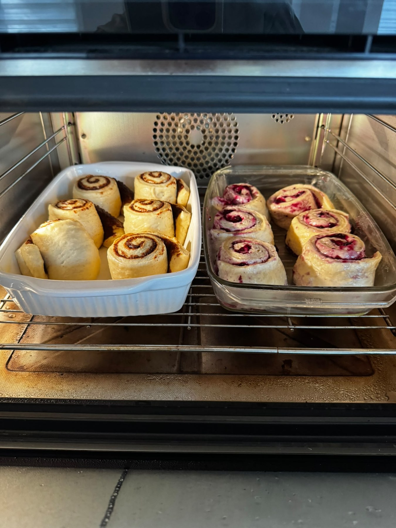 Zimt- und Blaubeerschnecken nebeneinander in zwei Formen im Backofen