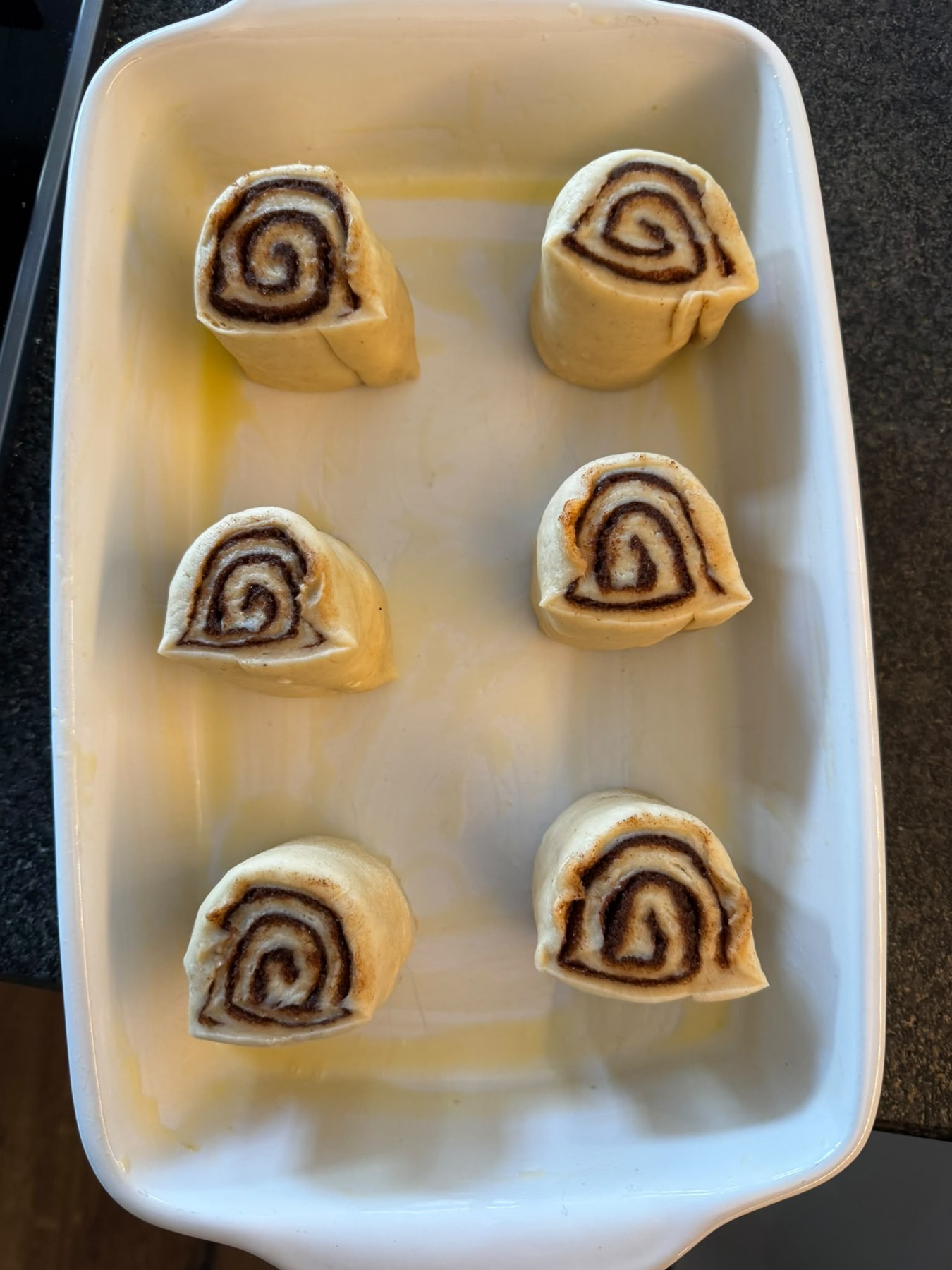 Sechs ungebackene Zimtschnecken mit Abstand in einer weißen Auflaufform